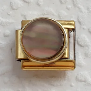 Dettaglio macro di un charm italiano in acciaio inossidabile dorato con pietra rosa