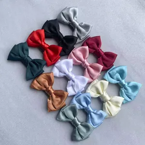 Assortment of eleven large satin bow clips in various colors arranged on textured fabric