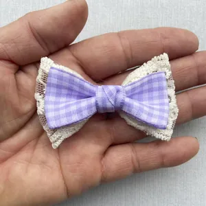 Detail of purple plaid bow accessory with white lace edges shown on a hand for scale