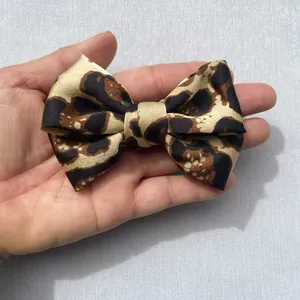Detalle de un lazo de satén con estampado de leopardo sostenido a mano para ver el tamaño