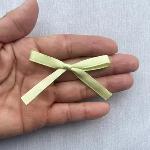 Mini-Schleife aus hellgrünem Satingewebe im Detail auf der Handfläche zur Skalierung