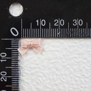 Detailed macro view of a 15mm light pink satin ribbon bow next to a measuring ruler scale