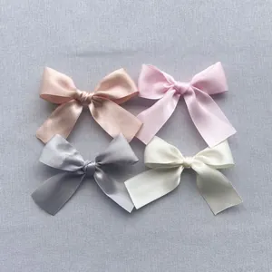 Detailed view of four satin bow hair accessories in pink, grey, and cream pastel colors