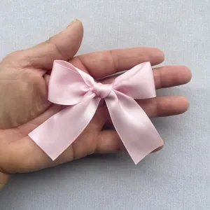 Close-up of small pink satin bow accessory on hand for size comparison and DIY hair decor