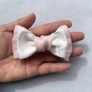 Detail of layered pink organza and white silk bow accessory held in hand for size
