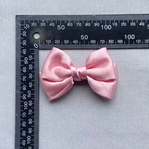 Detailed view of a pink satin decorative bow with dimensions shown on a ruler