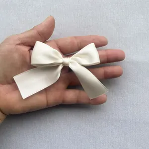 Close-up of a 7.5cm cream satin bow accessory held in hand for scale and texture detail