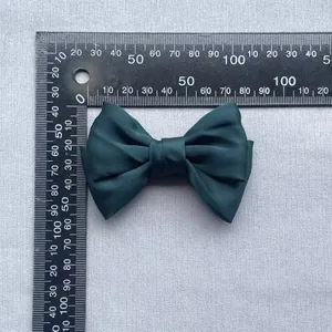 Detail of dark green satin bow accessory showing size measurement with a ruler