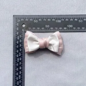 Detail view of pink and white satin bow showing 10cm width measurement with a ruler