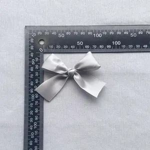 Macro detail of a 7.5cm grey satin ribbon bow accessory with ruler for size reference
