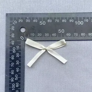 Detailansicht kleiner cremefarbener Satinschleifen mit Lineal zur 45 mm Maßstabsanzeige