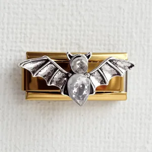 Vue détaillée du charme chauve-souris argenté avec strass blancs sur support doré