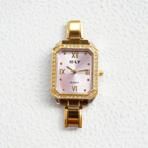 Dettaglio di un orologio dorato rettangolare con lunetta in cristallo e quadrante rosa