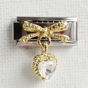 Macro view of gold bow and heart crystal charm on a silver modular link bracelet