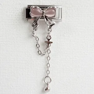 Macro detail of Italian charm bracelet link with pink bow and dangling cross pendant