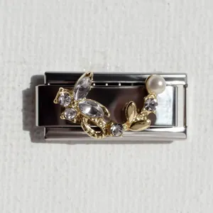 Dettaglio di un bracciale in acciaio inossidabile con fiori dorati, cristalli e perla bianca