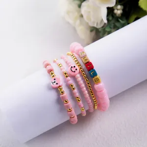Detail of five pink beaded bracelets with smile face charms and gold accents on a stand
