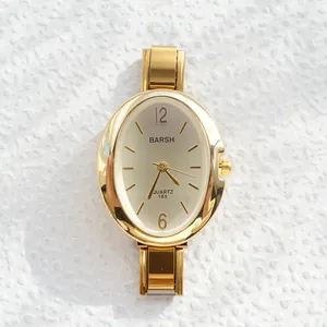Close-up of gold oval quartz watch with champagne dial on textured white stone