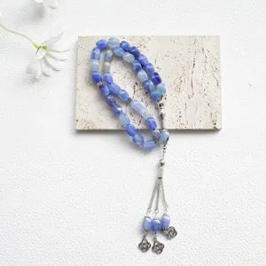 Tasbih islámico de ágata azul con borlas plateadas sobre una superficie de piedra clara