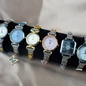 Orologi al quarzo di lusso da donna con cinturino in metallo e ciondoli su sfondo seta