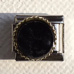 Macro shot of Italian charm bracelet link with black inlay and golden gear edge detail