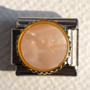 Macro detail of Italian modular charm link with pink marble insert and gold gear edge