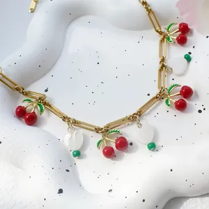 Detail van gouden schakelketting met 3D kersenhangers en witte hartvormige bedeltjes