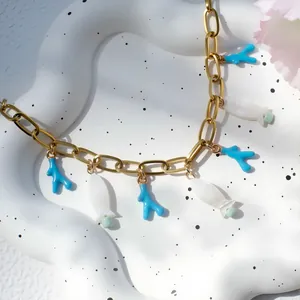 Detail van goudkleurige ketting met blauwe koraal- en witte visbedels op een dienblad