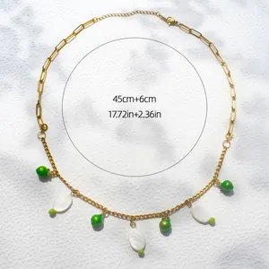 Detail van gouden ketting met groene kraal, schelphanger en lengtespecificaties in beeld