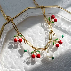 Macro-detail van gouden paperclip ketting met kersen en hartvormige emaille hangers