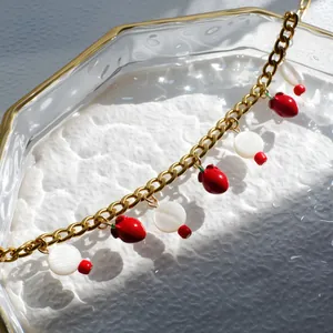 Detail van de gouden ketting met rode aardbei en witte schelp bedeltjes op een dienblad