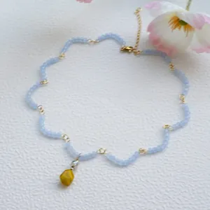Detail von hellblauen mattierten Perlen mit gelbem Anhänger und goldener Kette