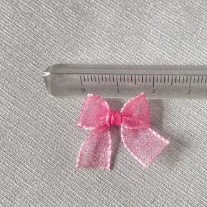 Detailed view of a 3cm pink organza bow charm measured with a ruler for DIY projects