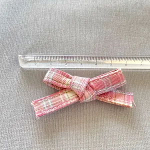 Detailed view showing a pink plaid bow being measured with a ruler at 5 cm