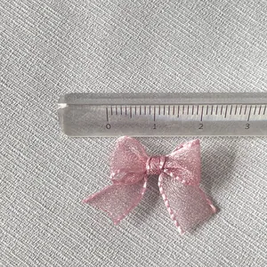 Macro shot of 2.5cm mini pink organza ribbon bow with glitter thread for DIY crafts