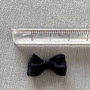 Mini black ribbon bow accessory showing 25mm size measurement on a gray woven background