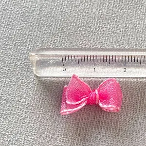 Close-up of a 20mm pink organza bow charm with delicate edging next to a clear ruler