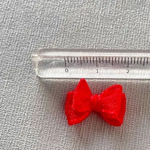 Close-up of a mini red ribbon bow next to a ruler showing its 21mm size for DIY crafts