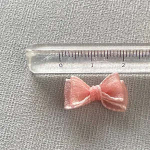 Close-up of a 2cm pink organza bow charm with a ruler showing exact size measurement