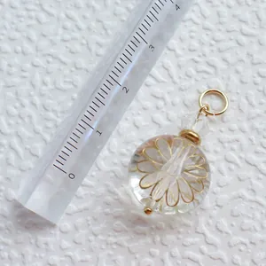 Detailansicht eines Glaskugel-Anhängers mit Goldblumen-Inlay und einem Messlineal dazu