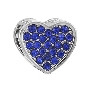 Macro detail of silver heart charm with blue pavé crystals and openwork carving