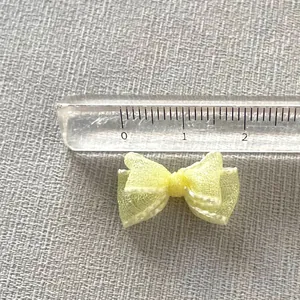 Macro detail of 2cm light yellow organza bow accessory with fine mesh texture and ruler