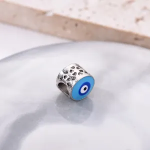 Silver hollow heart bead charm with blue evil eye detail on marble background