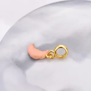 Pink croissant charm jewelry pendant with gold accents on marble background