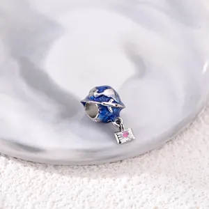 Blue globe charm with silver airplane and pink heart envelope pendant on marble surface