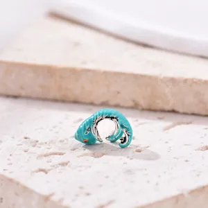 Macro view of a silver chameleon charm with teal enamel on a natural stone base