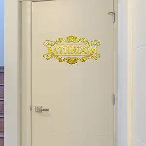 Λεπτομέρεια χρυσής ανάγλυφης πινακίδας Bathroom με φλοράλ σχέδια σε λευκή εσωτερική πόρτα
