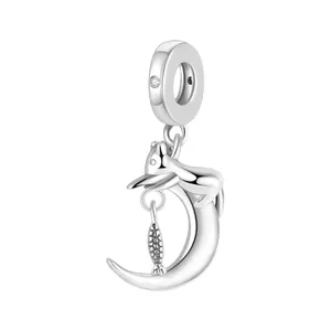 Macro detail of silver moon and cat charm with a dangling fish element and sparkling stone