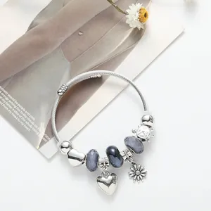 Silver charm bracelet with sunflower heart and purple glass beads on a magazine background