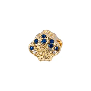 Détail macro du charm coquillage doré avec cristaux bleus et relief d'étoile de mer